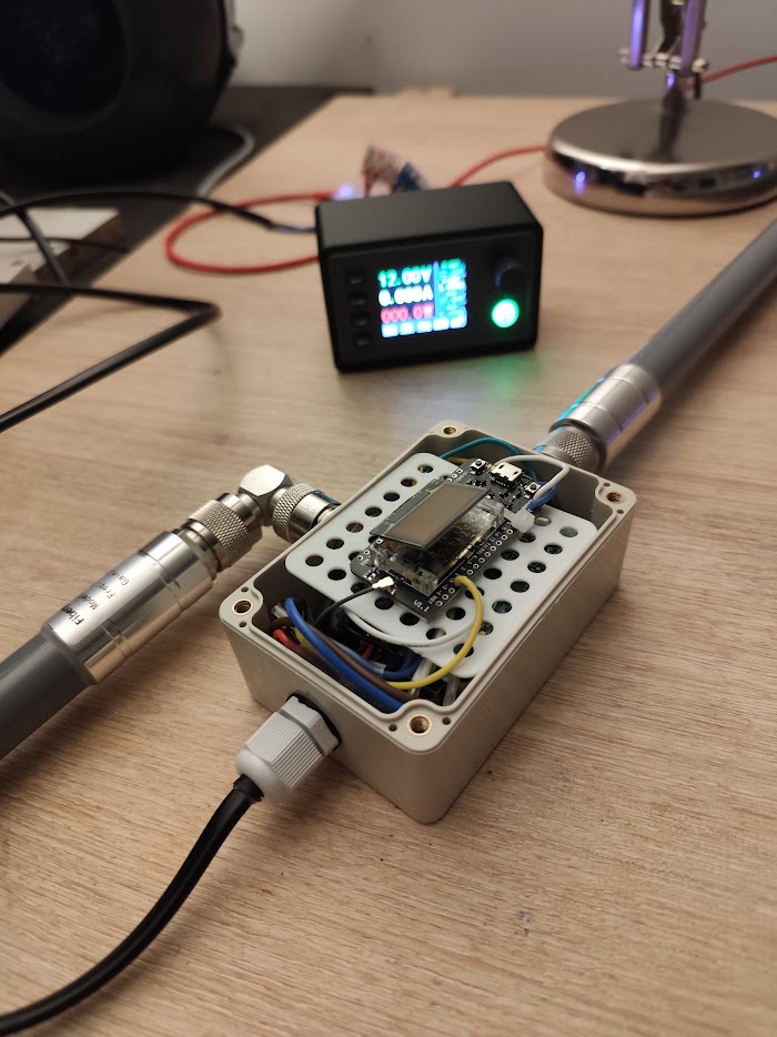 Relay gateway internals on the bench at 12 V, with a Heltec HTCC-AB02S CubeCell below the Pi reporting battery level and switching it on and off