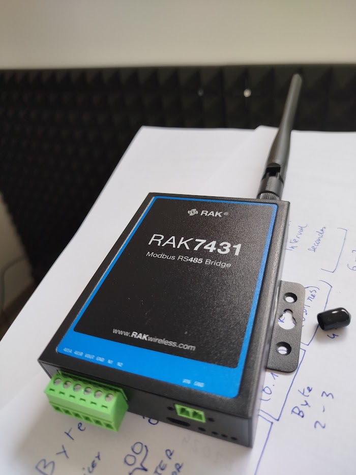 A RAK7431 Modbus RS485 to LoRaWAN bridge on the bench beside handwritten payload mapping notes